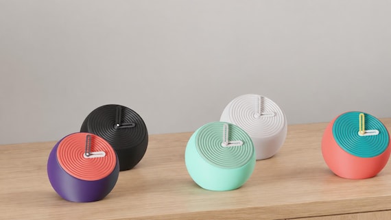 Alternate close-up of Pebblewave Spherical Desk Clock examples on light oak, showing their colored faces, hands and body profiles.
