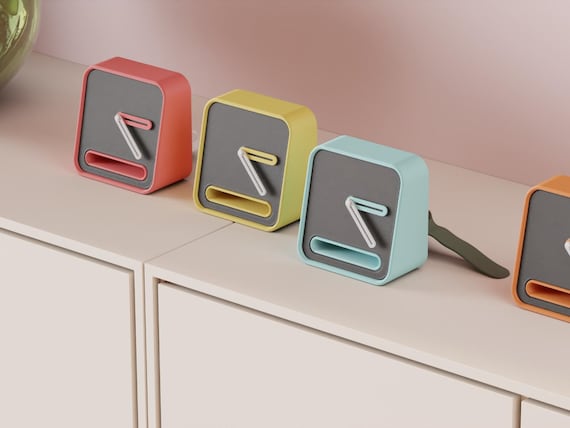 Slothour Desk Clock examples in contrasting colors on a pale cabinet, showing the finished clock faces and hands.