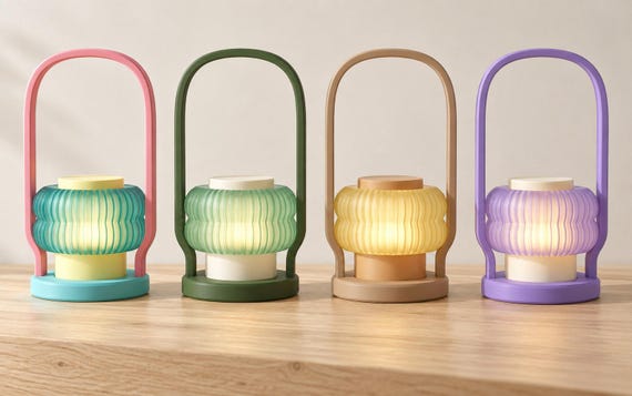 Four Harbor Glow lanterns on a wood tabletop, left to right: Coral Cove, Woodland Glow, Honey Dune and Twilight Bloom.