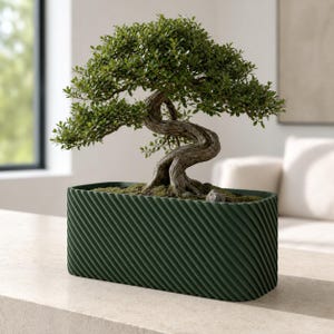 Może przedstawiać: Małe drzewko bonsai o skręconym, teksturowanym brązowym pniu i gęstych zielonych liściach, posadzone w prostokątnej ciemnozielonej doniczce. Doniczka posiada wyraźny wzór ukośnych żebrowań na zewnętrznej powierzchni, wypełniona ziemią i mchem.