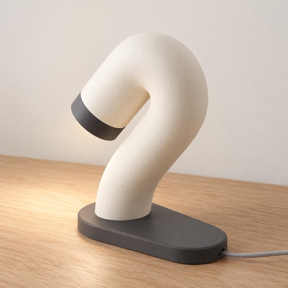 Rear three-quarter view of the Swayarc lamp in Ivory White and Charcoal, showing the flowing curve and cord exiting the oval base.