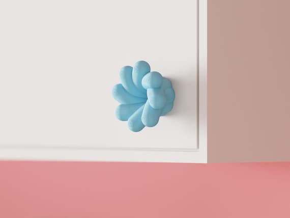 Blue petal-shaped cabinet knob on a white cabinet, angled view.