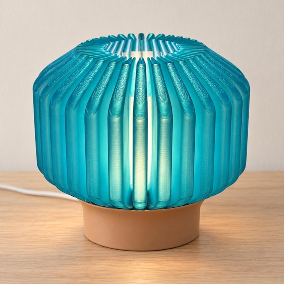 Coastal Cove Orivelle lamp with a Desert Tan matte base, glowing Teal ribbed outer shade and neutral inner diffuser on a pale wood tabletop.