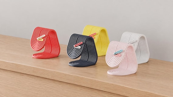 Angled close-up of Ribbonrise Sculptural Desk Clock examples in contrasting colors on light oak against a gray wall.