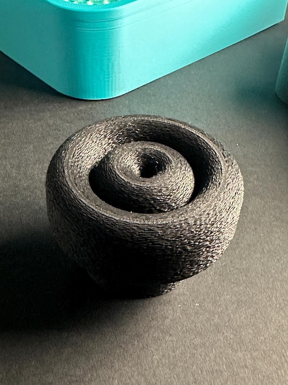 Black ring cabinet knob on a dark tabletop, showing its textured rounded surface.
