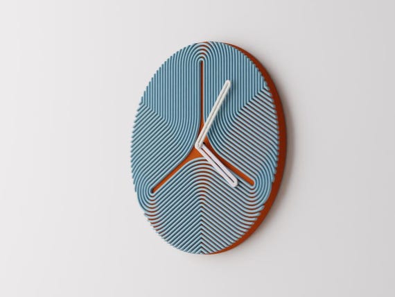 Triripple Wall Clock, blue curved ribs over a rust-colored round face with white hands, mounted on a pale wall in an angled view.