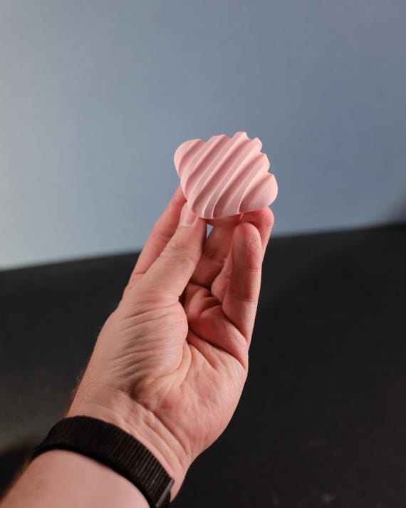 Pink ribbed cabinet knob held in a hand, showing its curved ridges from the front.