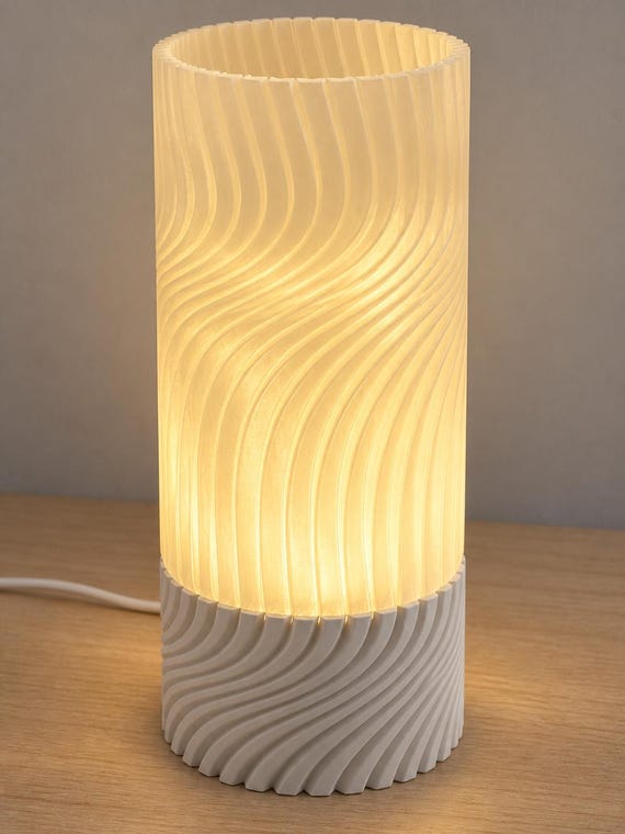 Linen Glow Seravelle lamp with a Bone White ribbed base and glowing Mellow Yellow spiral shade, open top and wired cord visible on a wood tabletop.