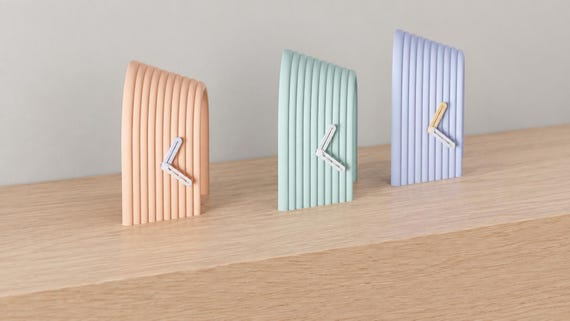 Angled close-up of Arcspan Sculptural Desk Clock examples in contrasting colors on light oak against a gray wall.