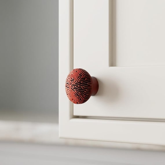 Terracotta textured cabinet knob on a paneled white cabinet, close angled view.
