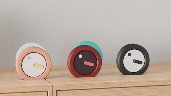 Angled close-up of Orbitmark Moving Face Clock examples in contrasting colors on light oak against a gray wall.