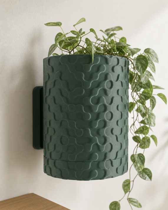 Close-up wall-mounted RippleGlyph planter in Dark Green with a trailing plant