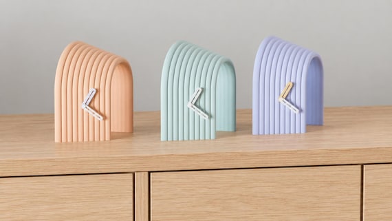 Alternate close-up of Arcspan Sculptural Desk Clock examples on light oak, showing their colored faces, hands and body profiles.