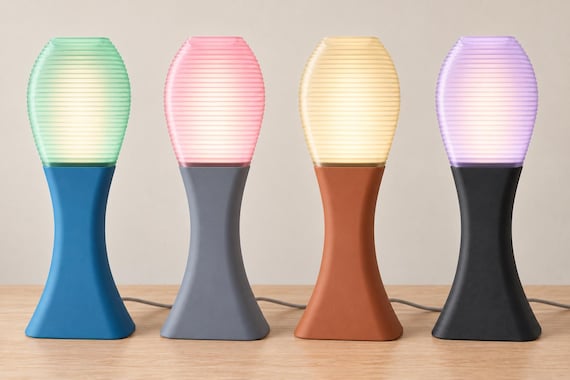 Four illuminated Arcelle lamps on a wood tabletop, left to right: Tidal Mist, Rose Quartz, Apricot Haze and Lilac Dusk.