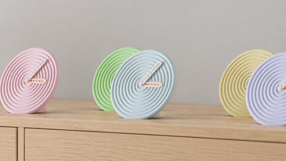 Alternate close-up of Rippledot Round Desk Clock examples on light oak, showing their colored faces, hands and body profiles.