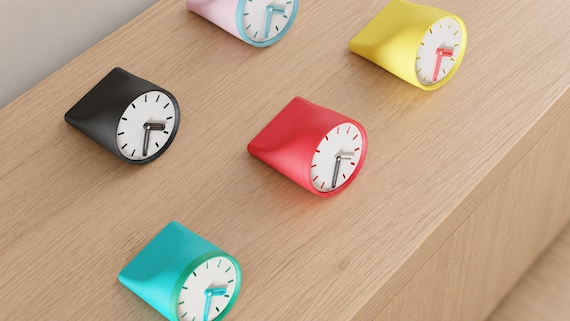 Angled close-up of Fincrest Desk Clock examples in contrasting colors on light oak against a gray wall.