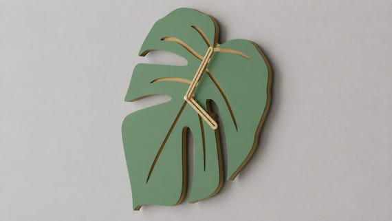 Verdant Vein Wall Clock, green leaf shape with tan veins and open tan hands, close-up on a gray wall from the source photograph viewpoint.