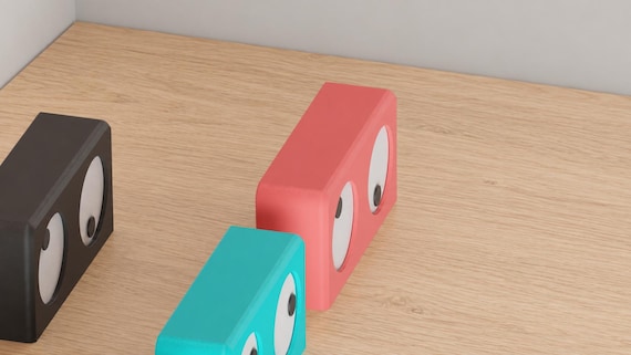 Wander Eyes Desk Clock examples in contrasting colors on oak, showing white eyes and dark pupils from an angled view.