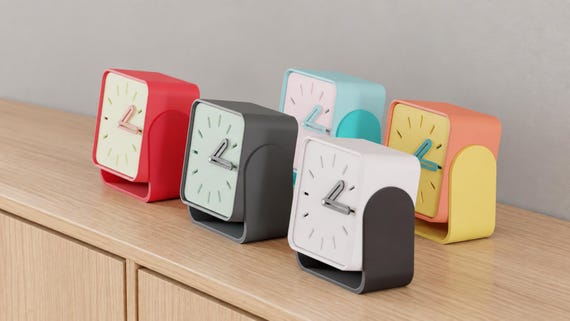 Alternate close-up of Pivotline Desk Clock examples on light oak, showing their colored faces, hands and body profiles.