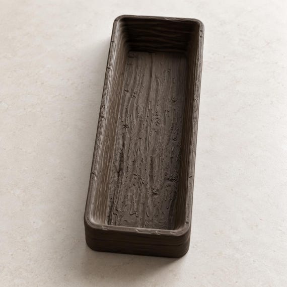 Empty espresso brown Timberfold valet tray showing its long narrow basin and molded grain from above on a light tabletop