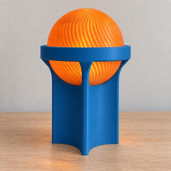Sunset Cove Orbessa lamp with a Marine Blue matte base and ring and softly glowing Orange ribbed globe on a pale wood tabletop.