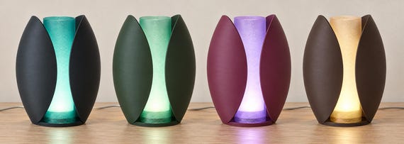 Four illuminated Lunafold lamps on a wood tabletop, left to right: Midnight Tide, Forest Mist, Plum Glow and Cocoa Amber.
