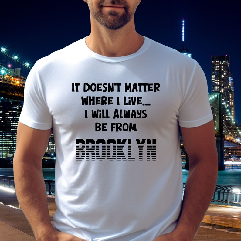 May include: White t-shirt with black text that reads "It doesn't matter where I live... I will always be from Brooklyn". The text "Brooklyn" is in a stylized font with black horizontal lines.