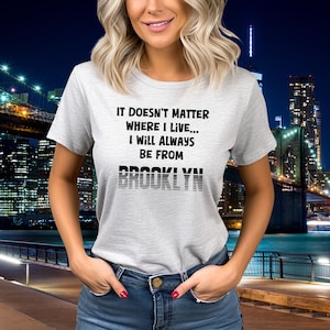 May include: A gray t-shirt with black text that reads "It doesn't matter where I live... I will always be from Brooklyn". The text "Brooklyn" is in a stylized font with black lines.