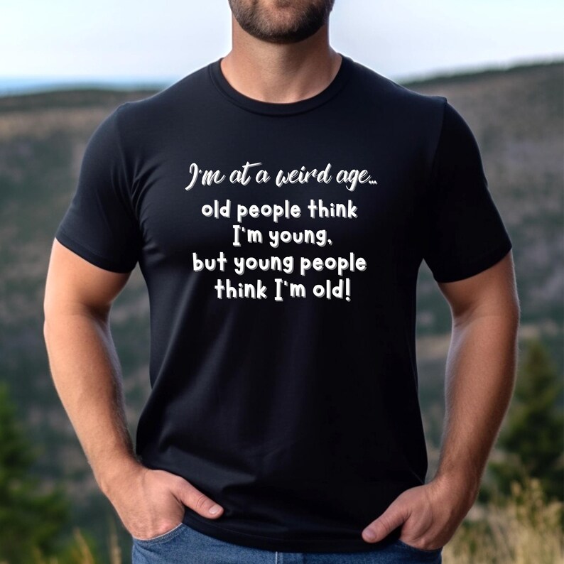 Puede incluir: Una camiseta negra con texto blanco que dice "Estoy en una edad extra&ntilde;a... la gente mayor piensa que soy joven, pero la gente joven piensa que soy viejo!"