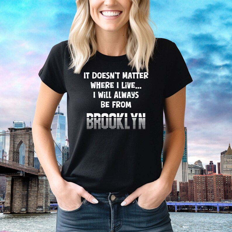 May include: Black t-shirt with white text that reads "It doesn't matter where I live... I will always be from Brooklyn". The text is in a retro style font with white stripes.