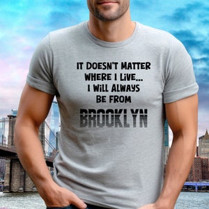 May include: A gray t-shirt with black text that reads "It doesn't matter where I live... I will always be from Brooklyn". The text "Brooklyn" is in a stylized font with horizontal lines.