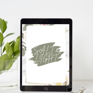 Op de afbeelding: Een digitale tablet met een witte achtergrond en de tekst "SALT & LIGHT" in een groen penseelstreepontwerp. De tablet is omringd door een bloemige rand.