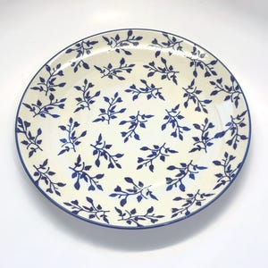 May include: A white ceramic dinner plate with a blue floral pattern. The plate has a blue rim.