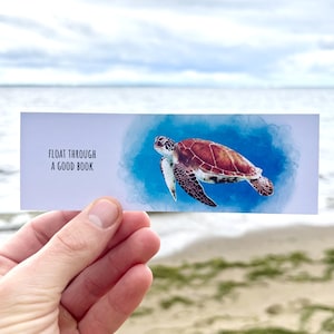 May include: A bookmark featuring a watercolor illustration of a sea turtle swimming in blue water. The text "FLOAT THROUGH A GOOD BOOK" is printed on the bookmark.