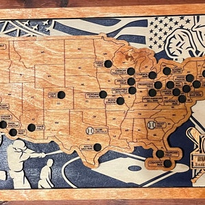 May include: Wooden baseball travel map featuring the United States with baseball stadium locations marked. The map includes the text "BUSH FAMILY BASEBALL TRAVEL MAP" and baseball-themed illustrations. The frame is a light brown color.