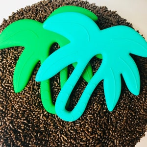 May include: A close-up shot of a dessert covered in chocolate sprinkles, with three palm tree-shaped decorations in shades of green and teal. The decorations are made of a smooth, solid material and are arranged on top of the sprinkles.
