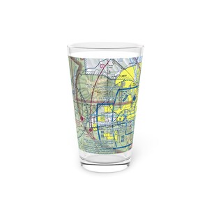 May include: A clear glass pint glass with a yellow and green airport map printed on it. The map shows the area around "SUN CITY WEST" with the text "SPECIAL AIR TRAFFIC RULE" and "PHOENIX SKY HARBOR" printed on the map.