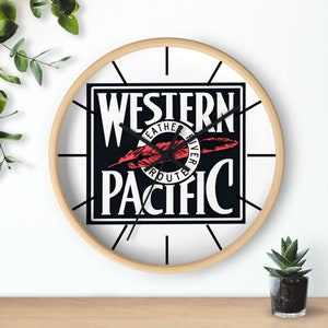 Puede incluir: Un reloj redondo de madera con agujas negras y una cara blanca. La cara del reloj presenta un logotipo en blanco y negro con el texto "Western Pacific" y un gráfico de pluma roja.
