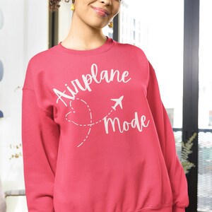 May include: A pink sweatshirt with the text "Airplane Mode" in white lettering. The text is accompanied by a stylised airplane and a heart with a dashed line.