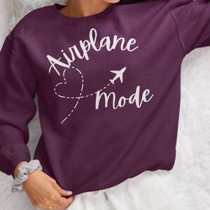 May include: A purple sweatshirt with the text "Airplane Mode" in white lettering. The text is accompanied by a stylised airplane and a heart with a dashed line.