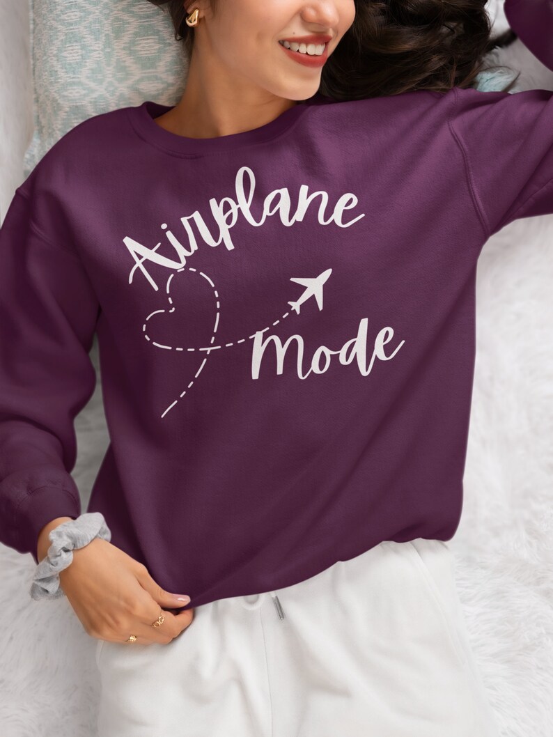 May include: A purple sweatshirt with the text "Airplane Mode" in white lettering. The text is accompanied by a stylised airplane and a heart with a dashed line.