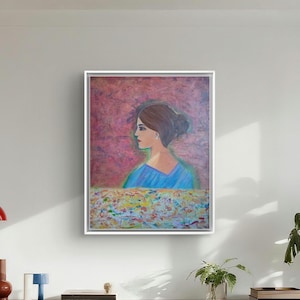 Puede incluir: Un cuadro enmarcado que representa el perfil de una persona con el pelo castaño recogido en un moño, vistiendo una prenda azul. El fondo es de color magenta texturizado, mientras que la parte inferior del lienzo presenta un patrón abstracto y colorido.