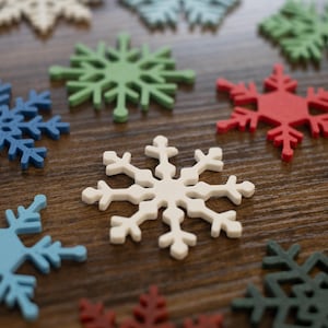 May include: A selection of colourful snowflake ornaments in shades of blue, green, red, and white. The snowflakes are arranged on a wooden surface, creating a festive and decorative display. Perfect for holiday decorations.
