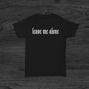 Pu&ograve; includere: Maglietta nera con il testo "leave me alone" in font gotico bianco.