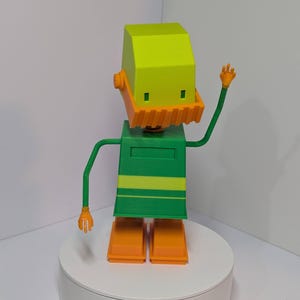 May include: A 3D-printed robot figurine with a lime green head and body, orange beard, hands, and feet. The robot has a green body with yellow stripes and is posed with one arm raised in a waving gesture. The figurine is standing on a white circular base.