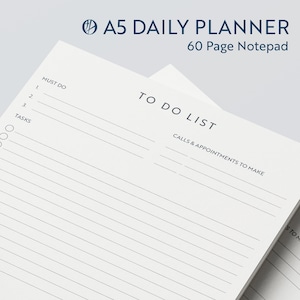May include: A white A5 daily planner notepad with a blue title "A5 DAILY PLANNER 60 Page Notepad". The notepad has a to-do list section with the text "TO DO LIST" and "CALLS & APPOINTMENTS TO MAKE".