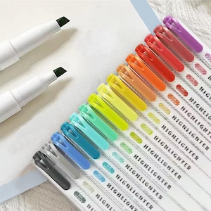 May include: A set of 15 colourful highlighter pens with clear plastic barrels and black caps. The pens are arranged in a rainbow order, with the darkest colours at the top and the lightest colours at the bottom. The text "HIGHLIGHTER" is printed on each pen.