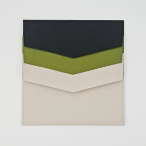 May include: A set of three envelopes in black, green, and beige. The envelopes are nested inside each other, with the black envelope on top and the beige envelope on the bottom.