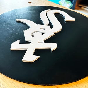 May include: A black circular sign with a white stylized Japanese character in the center. The character is raised and appears to be made of foam.