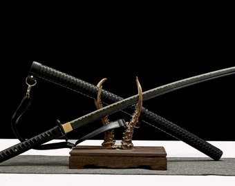 Puede incluir: Una katana negra con una vaina negra, expuesta en un soporte de madera con detalles de asta de ciervo. La espada está cruzada sobre la vaina.
